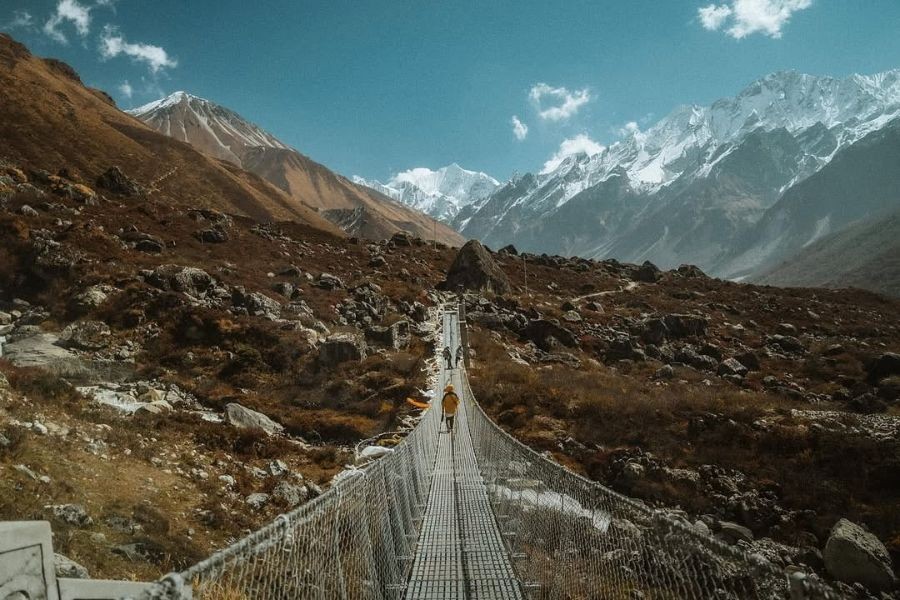Trekker crossing suspension bridge with snow-capped Himalayan peaks in Langtang
